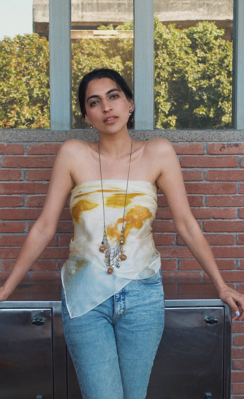 Woman wearing a sleeveless top with a floral pattern and blue jeans standing against a brick wall.