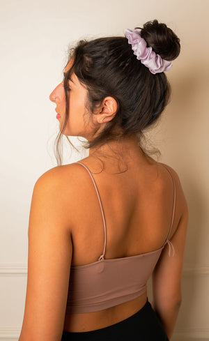 Woman wearing a beige top with thin straps, standing against a plain wall.