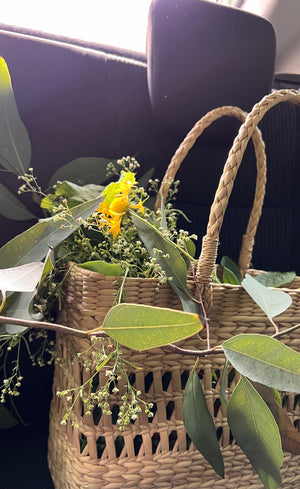 A woven basket overflowing with fresh eucalyptus leaves and yellow wildflowers - botanicals gathered for eco-printing at Jasmine Bains