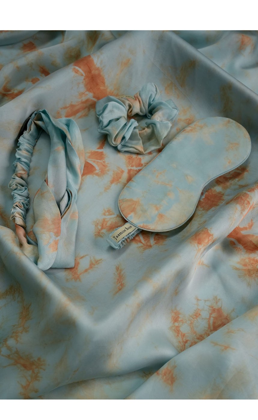 Tie-dye hair accessories including a headband, scrunchies, and a paddle on a tie-dye fabric background.