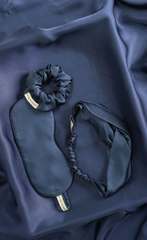 Navy blue sleep mask, scrunchie, and eye mask set on a dark fabric background