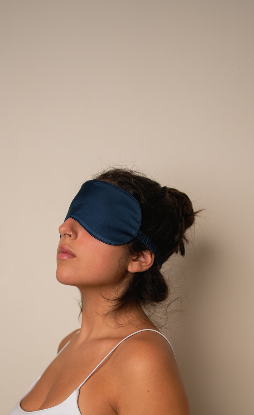 Navy blue sleep mask, scrunchie, and eye mask set on a dark fabric background