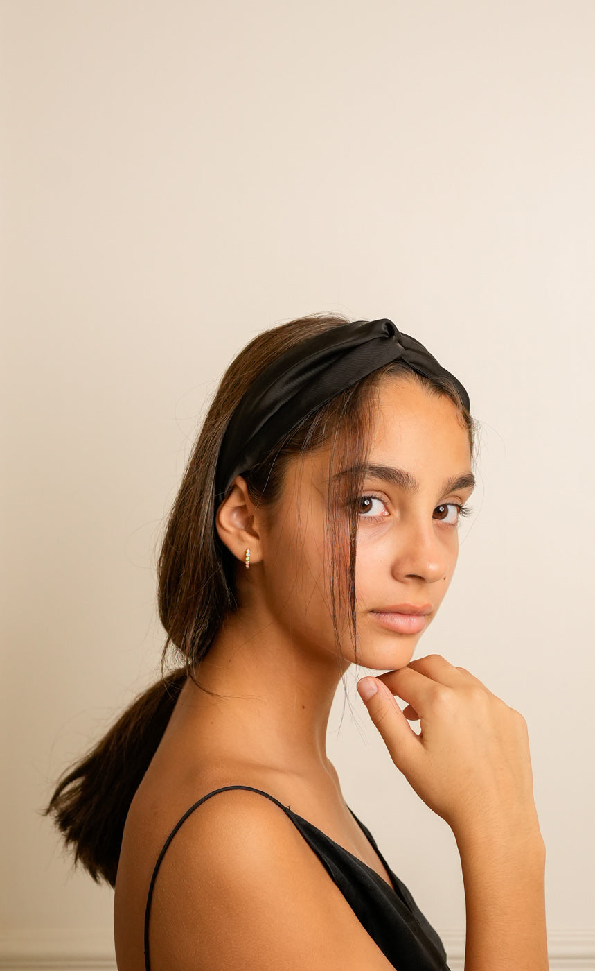 Woman wearing a black satin headband against a beige background