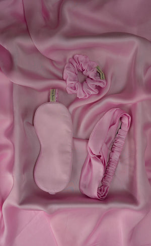 Luxurious pink sleep mask, scrunchie, and headband on a pink satin background
