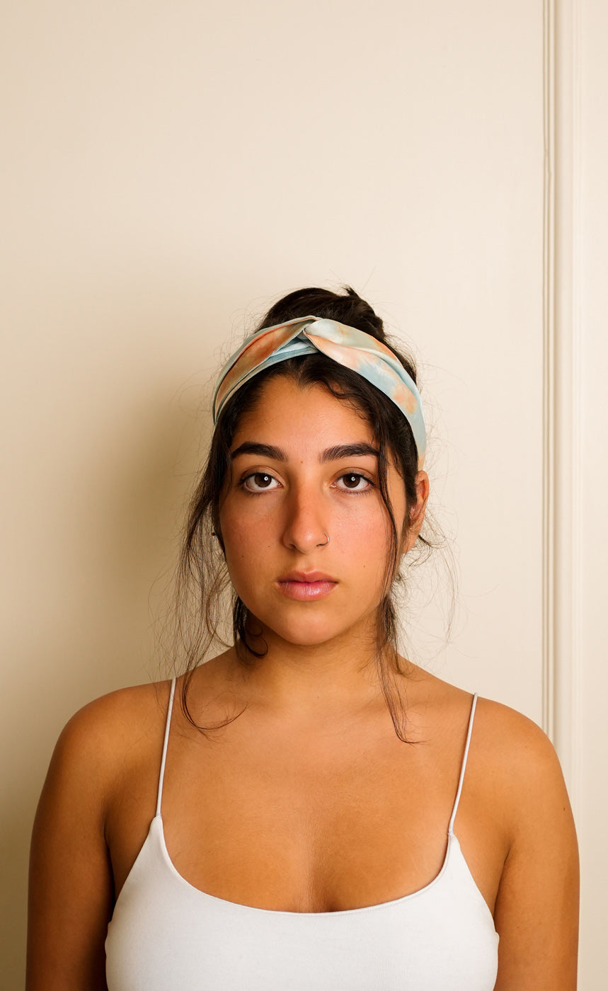 Woman wearing a blue tie and dye marble print headband against a beige wall