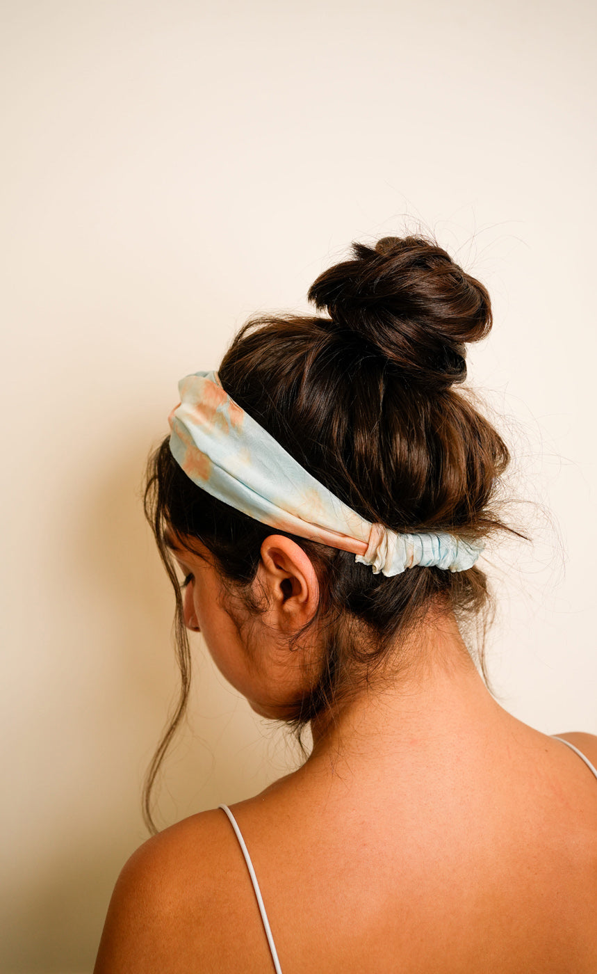 Woman wearing a blue tie and dye marble print headband against a beige wall