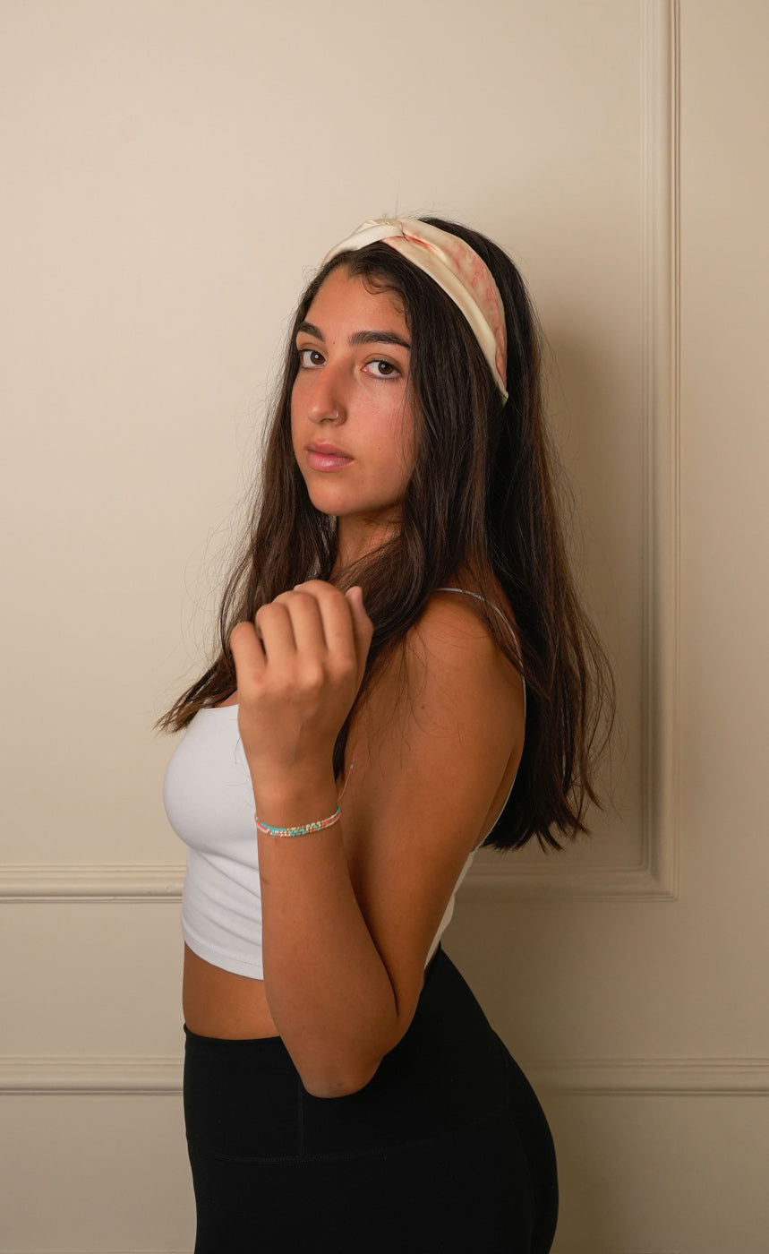 Woman wearing a tie and dye marble electric beige and rust peach headband against a beige wall.