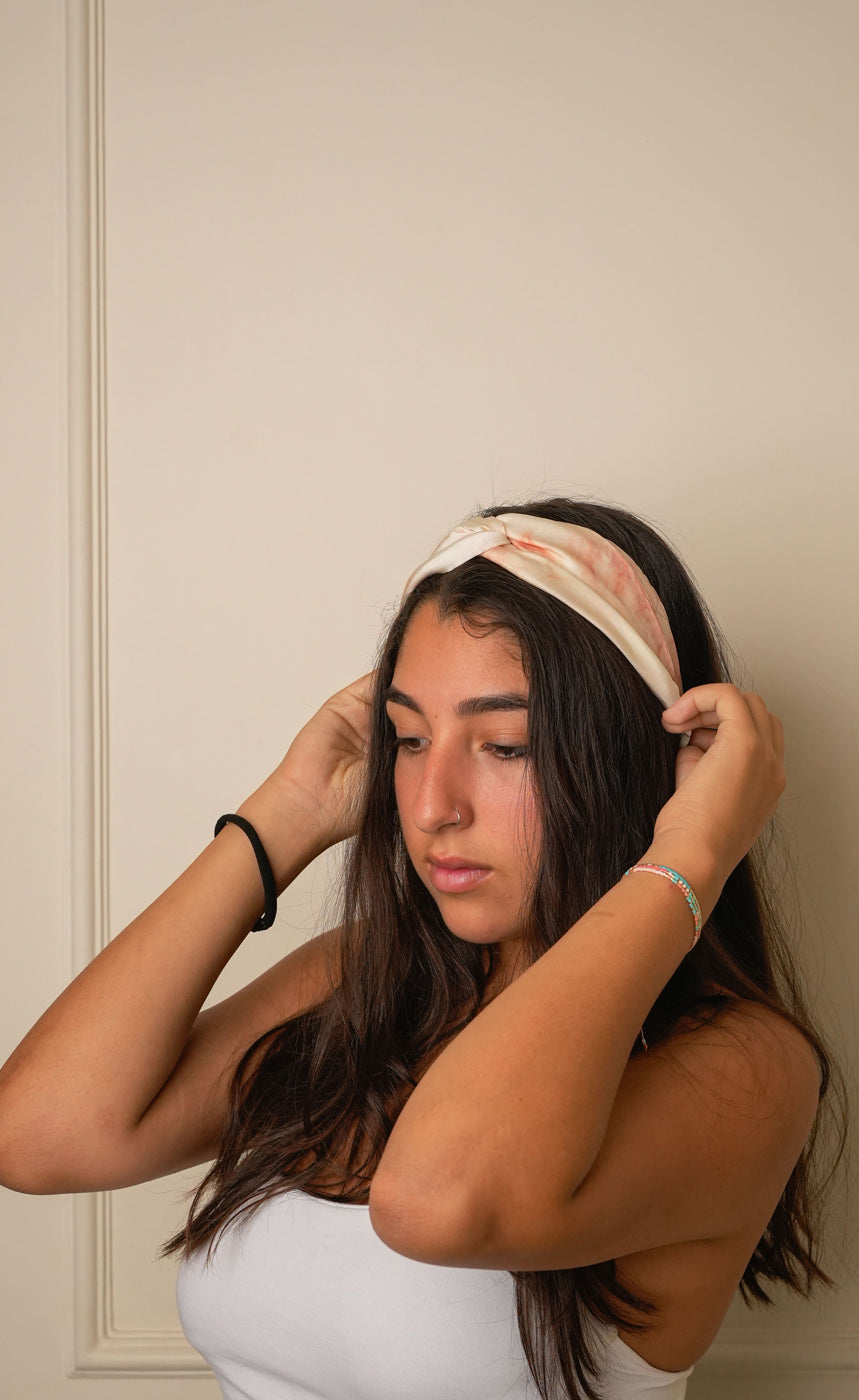 Woman wearing a tie and dye marble electric beige and rust peach headband against a beige wall.