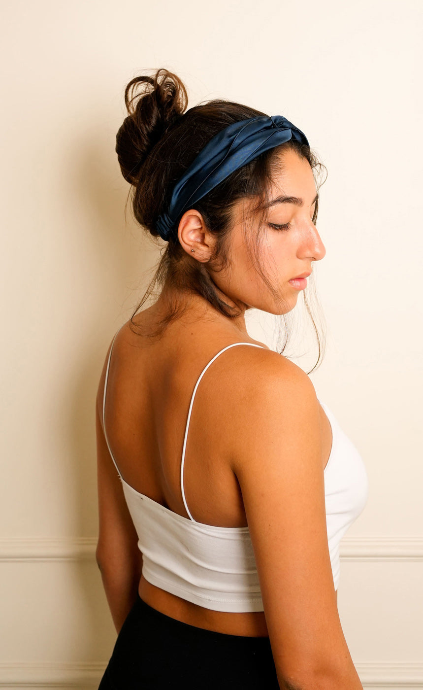 Woman wearing a blue knotted satin headband against a light coloured wall. 