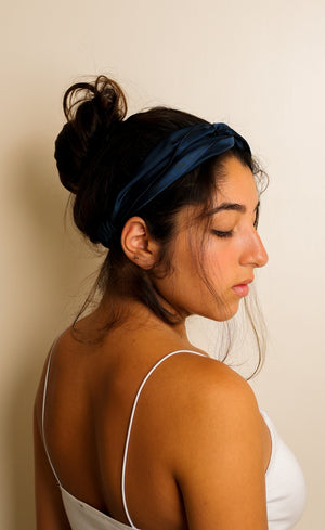 Woman wearing a midnight blue satin headband against a plain background