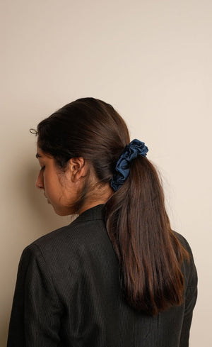 Person with a blue scrunchie in their hair against a beige background