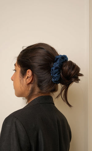 Person with a blue scrunchie in their hair against a plain background