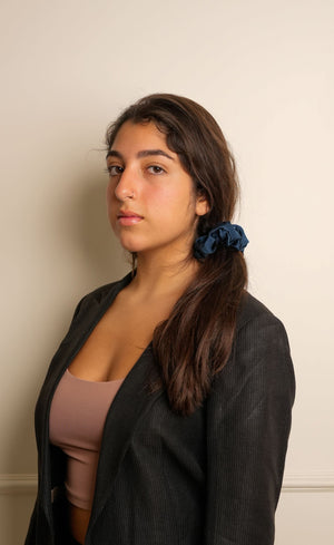 Woman with a blue scrunchie in her hair against a plain wall