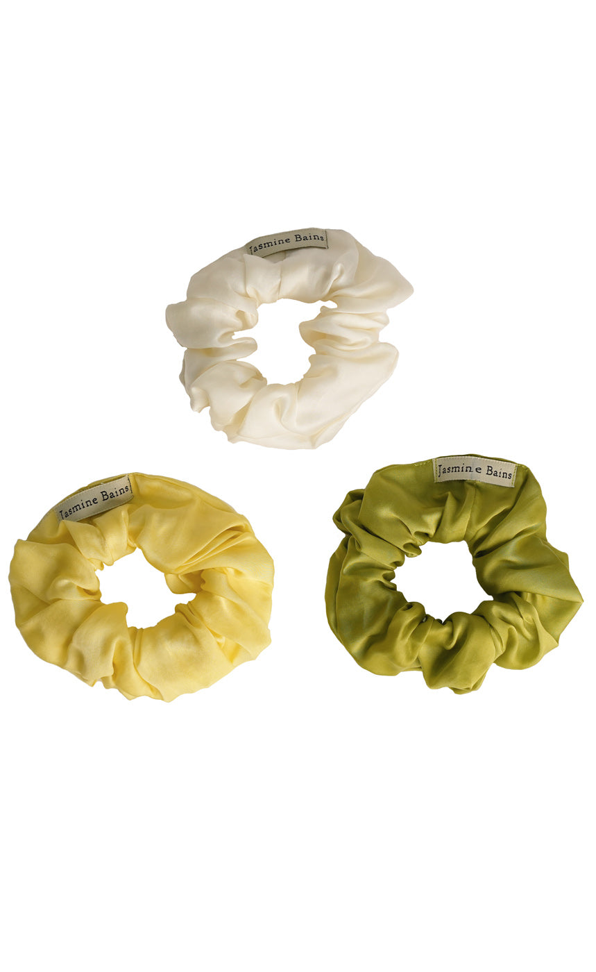 Three satin scrunchies in cream, yellow, and green on a white background.