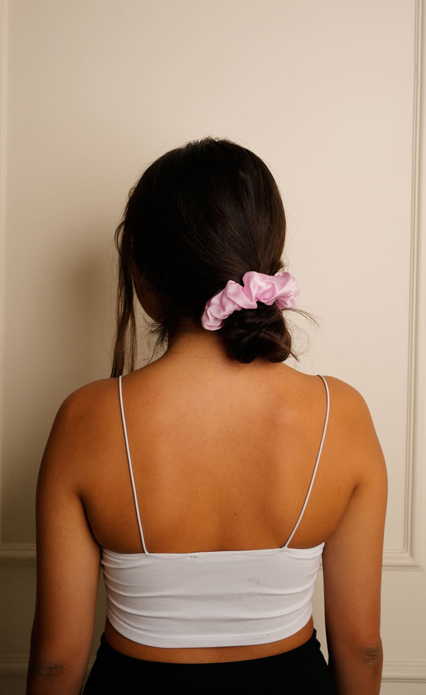 Person wearing a white top with thin straps, standing against a neutral wall.