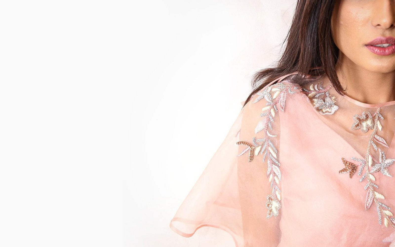 Woman wearing a light pink outfit with floral embellishments on a white background