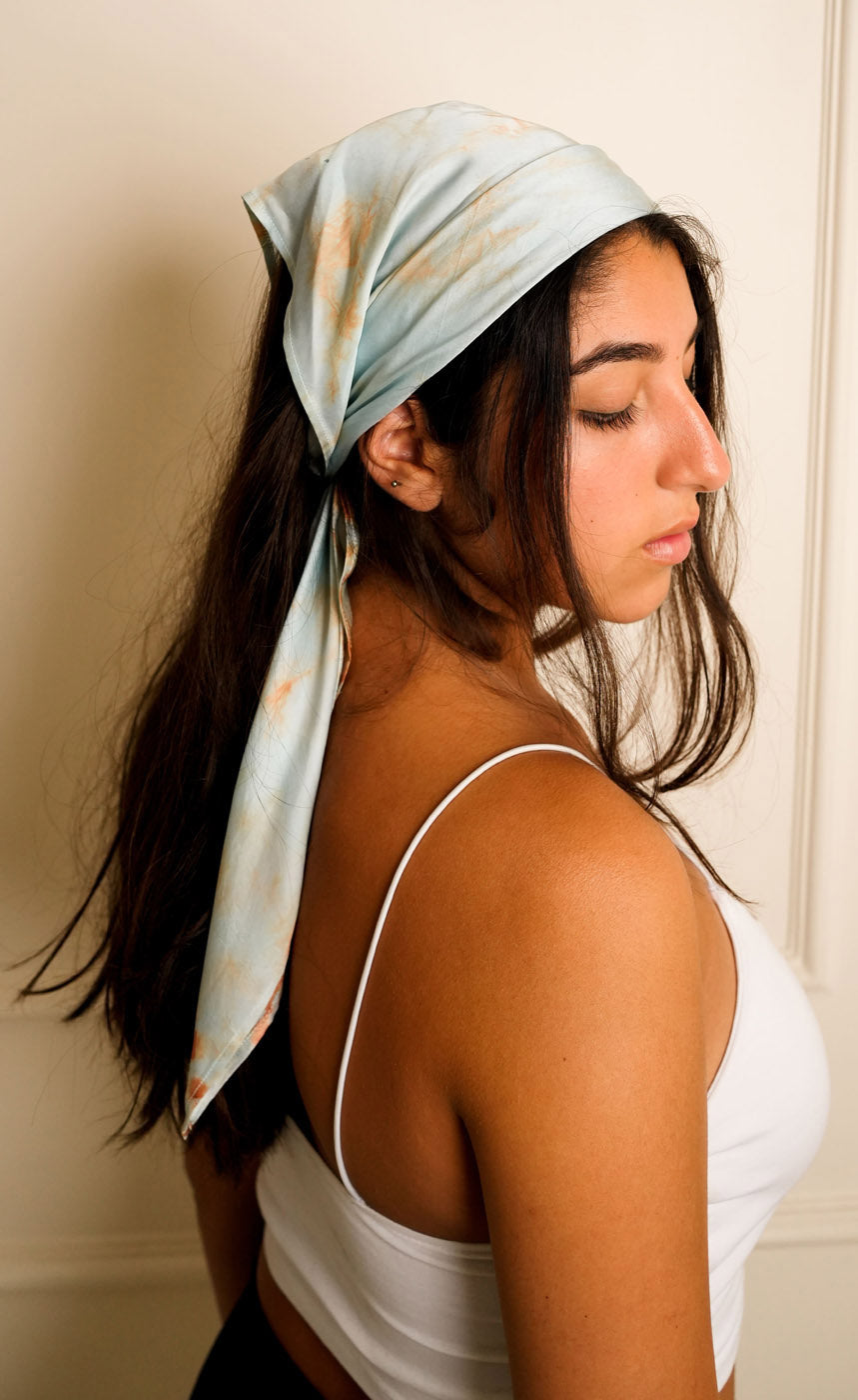 Woman wearing a light blue headscarf with floral patterns on a beige background