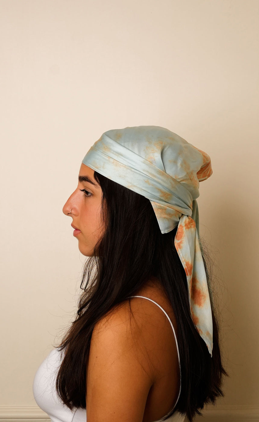 Woman wearing a light blue headscarf with floral patterns on a beige background