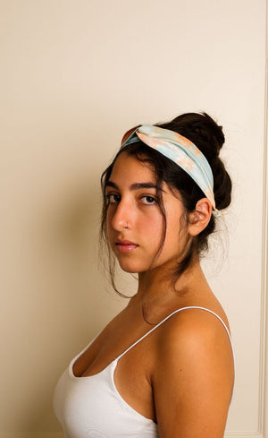 Woman wearing a white tank top and a headband with a pattern against a beige wall