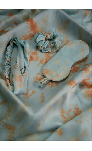 Set of scrunchies, eye mask and a knotted head band on a tie-dye fabric background. 