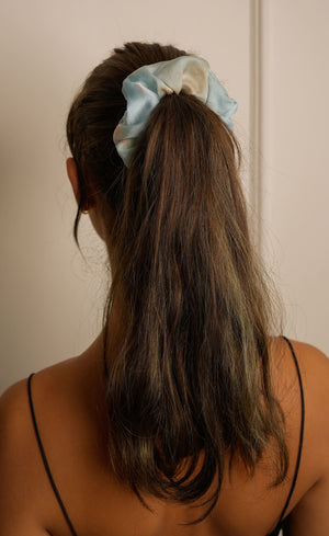 Person with a ponytail held up with a light blue scrunchie against a plain background