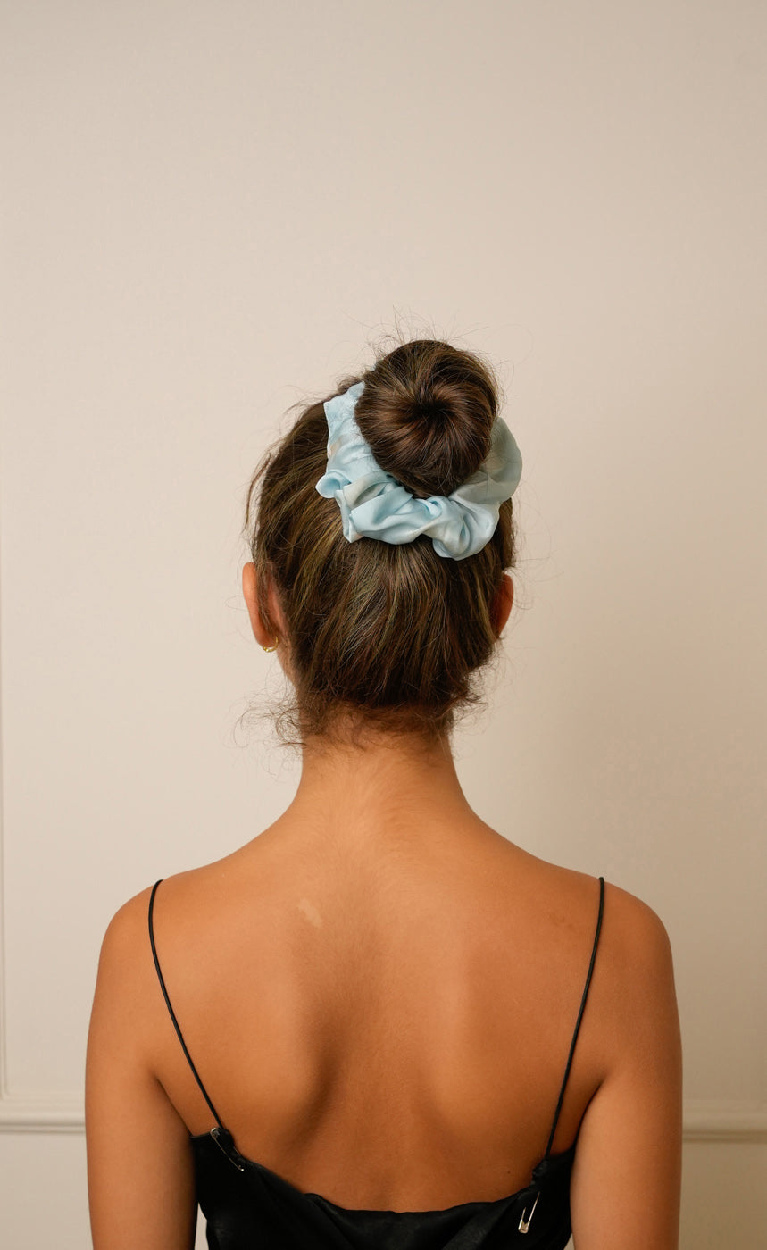 Person with a blue scrunchie in their hair against a beige background