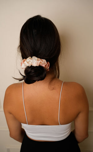 Person with a scrunchie in their hair wearing a white top against a plain background