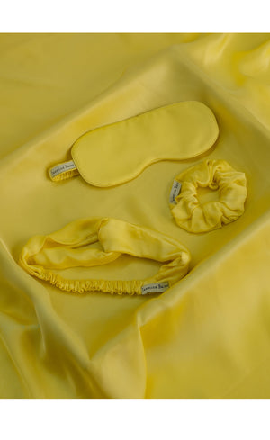 Yellow satin eye mask and hair tie set on a yellow satin background