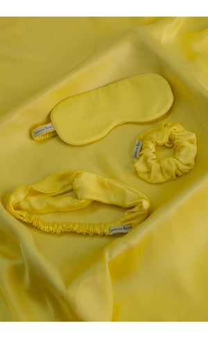 Yellow satin eye mask, headband, and scrunchie set on yellow fabric