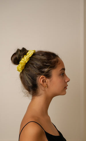 Woman with a yellow scrunchie in her hair against a plain background