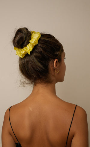 Woman with a yellow scrunchie in her hair against a plain background