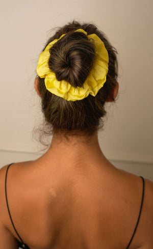 Person with a yellow hair scrunchie in their bun against a plain background