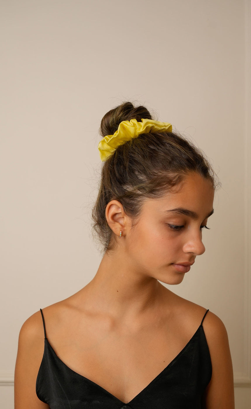 Person with a yellow hair scrunchie in their bun against a plain background