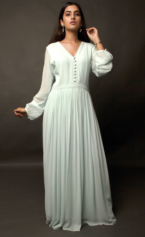 The muse is wearing our gathered pin tucked floor length dress in cupro georgette in aqua green shade. There's a substantial button detail V-neckline accompanied with lace enhancement on neck. The dress is further enhanced with gathered full statement sleeves and is given a finished look with yoke along the waistline adding up to the whole look of the apparel.