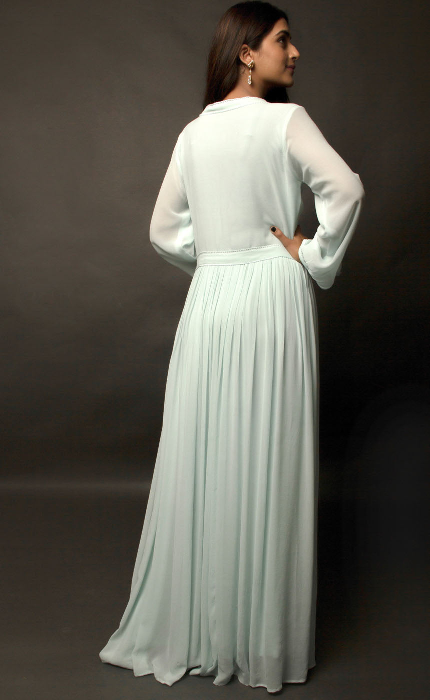 The muse is wearing our gathered pin tucked floor length dress in cupro georgette in aqua green shade. There's a substantial button detail V-neckline accompanied with lace enhancement on neck. The dress is further enhanced with gathered full statement sleeves and is given a finished look with yoke along the waistline adding up to the whole look of the apparel.