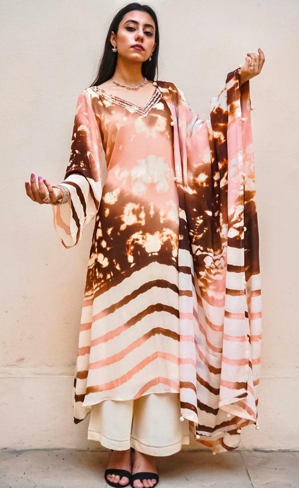 This signature tie-dye kurta set offers a beautiful abstract blend of twin dye technique split between the upper and the lower half of the garment. The blend of abstract dye on the top with accents of blush, copper and rust, represents the colourful sunsets of Mykonos balancing with the calming waves at the bottom half. 