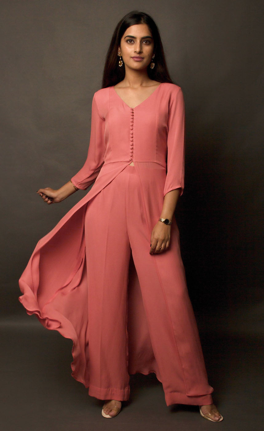 The muse here is wearing a simple and elegant front-slit dress with palazzos in carrot pink. The dress comprises of an upper yoke and a simple v-neckline which is further having a vertical buttoned detail on yoke and a high slit in the middle center. It is further paired with cupro georgette flowy wide legged palazzos.