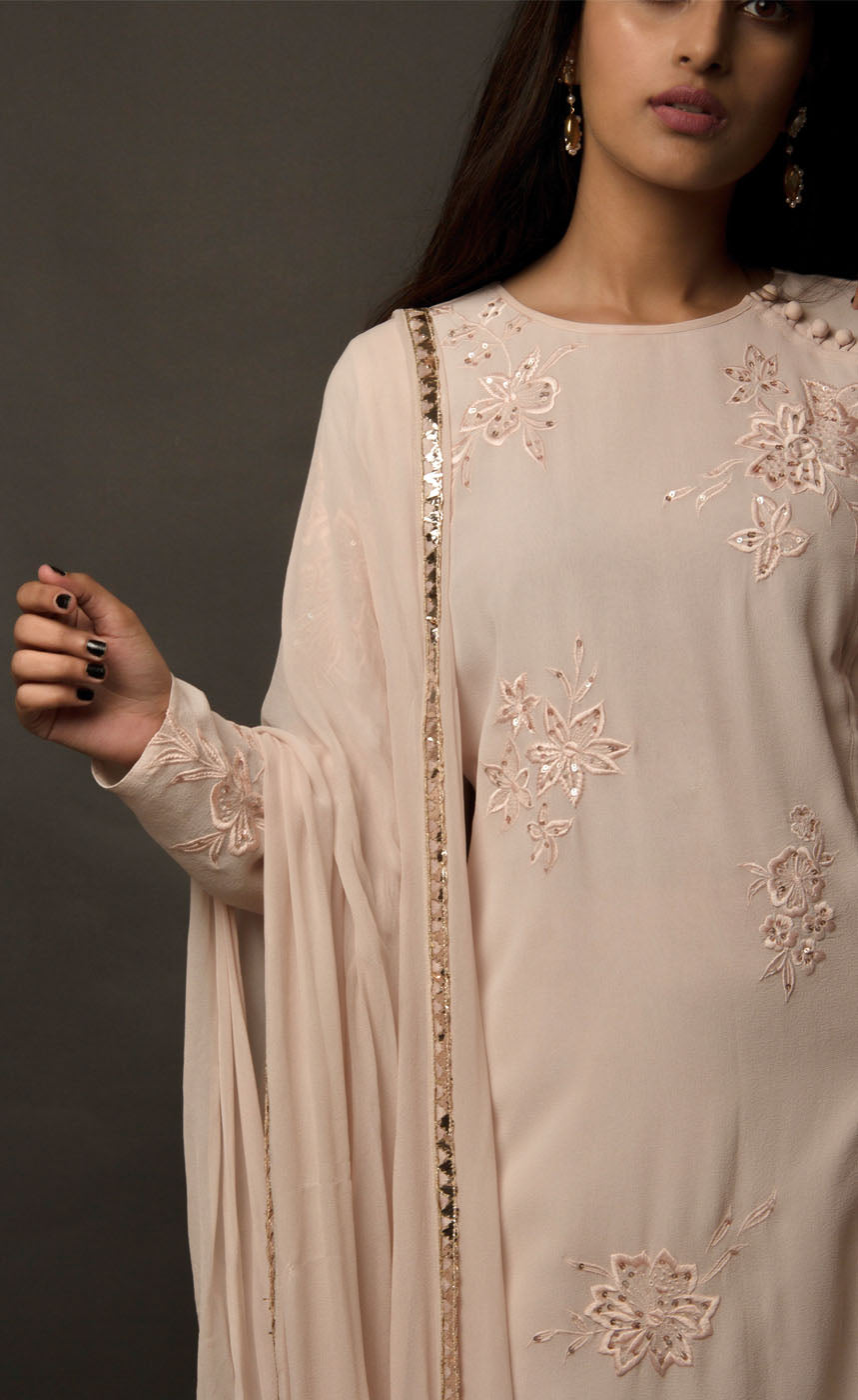 Dusty Rose side slit suit set, crafted in georgette, fully embroidered with signature flat threadwork topped with sequins spray accompanied by a dupatta with rose gold mukaish border. The ensemble carries a strong of a confident style because of the slim straight trousers underneath, the bottom of the trousers is finished by our signature buttoned hemline style. Flaunt your chic style in this elaborately worked ensemble, the muse radiates a modern, yet classic vibe. 