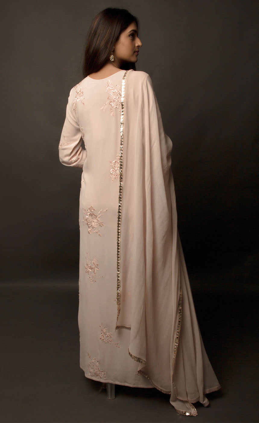 Dusty Rose side slit suit set, crafted in georgette, fully embroidered with signature flat threadwork topped with sequins spray accompanied by a dupatta with rose gold mukaish border. The ensemble carries a strong of a confident style because of the slim straight trousers underneath, the bottom of the trousers is finished by our signature buttoned hemline style. Flaunt your chic style in this elaborately worked ensemble, the muse radiates a modern, yet classic vibe. 