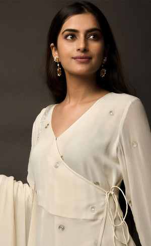 The muse is seen here wearing a classic angrakha style kurta suit set, delicately hand embroidered with a steel grey tilla. The motifs are scattered all over the front and back of this ivory angrakha set in georgette. The double bell sleeve with a beautiful flare, is a little modern play here in this classic angrakha silhouette. The silhouette is paired with wide legged easy palazzos and a dupatta embellished with tonal grey beadwork border. 
