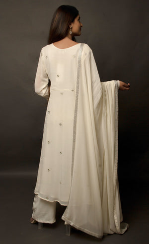 The muse is seen here wearing a classic angrakha style kurta suit set, delicately hand embroidered with a steel grey tilla. The motifs are scattered all over the front and back of this ivory angrakha set in georgette. The double bell sleeve with a beautiful flare, is a little modern play here in this classic angrakha silhouette. The silhouette is paired with wide legged easy palazzos and a dupatta embellished with tonal grey beadwork border. 