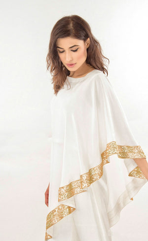 The muse here is wearing our effortlessly elegant ivory cape dress. This is a silk asymmetrical one shoulder cape which is intricately embroidered with sequins along the flowy flared border of the cape, which is further paired with straight trousers with metal buttons finishing on the bottom cuff sides. Perfect for every occasion, this stunning outfit will make you dazzle and look your best.