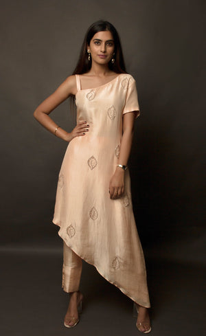The muse is seen wearing a beautiful asymmetrical flared dress in powder peach. There is a traditional mango motif crafted in glass beads all over the front and the back of the dress. Little details like the anchor thread-work over the small strap are intricate details that only a wearer can enjoy. This ankle length dress is perfectly paired with our signature buttoned pants. This glamorous outfit with these enhanced elements is a perfect outfit for any event. 