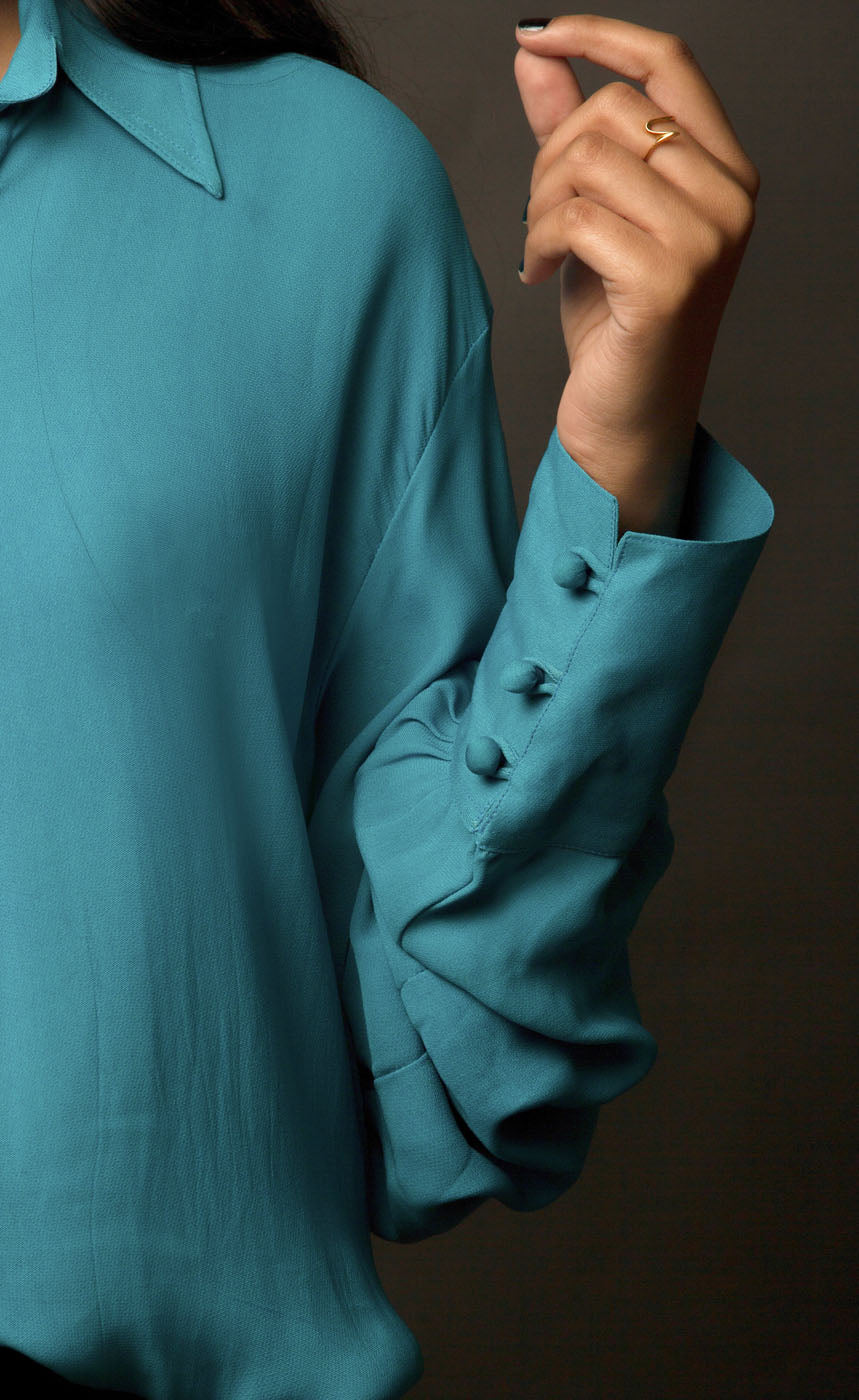 This peacock blue-green classic loop-buttoned business shirt crafted in cupro georgette, with gathered full sleeves, focuses on the modern muse and exudes a sophisticated touch of classic. With its beautiful drop shoulders, it adds a sense of creativity to your shirt style.  