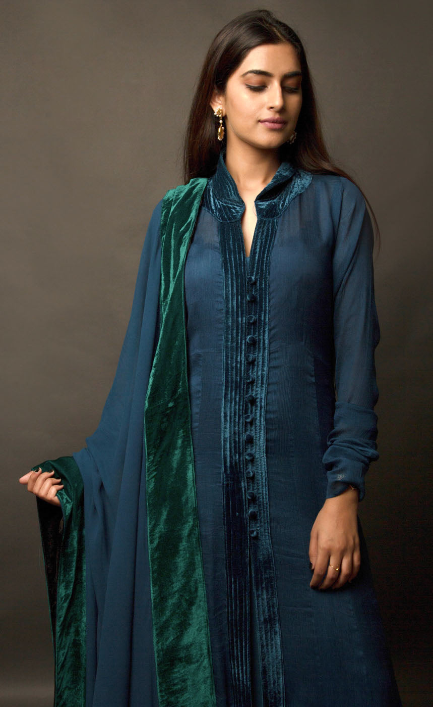 This is a beautiful plush velvet peacock blue-green long dress. It is a silk chiffon panelled dress with wrinkled sleeves, having a standing mandarin collar neckline and buttoned silk velvet placket. It is further lined with a taffeta slip having a cushioned yoke. It is accompanied by a silk georgette shawl finished with contrasting soft moss and sapphire black silk velvet borders.