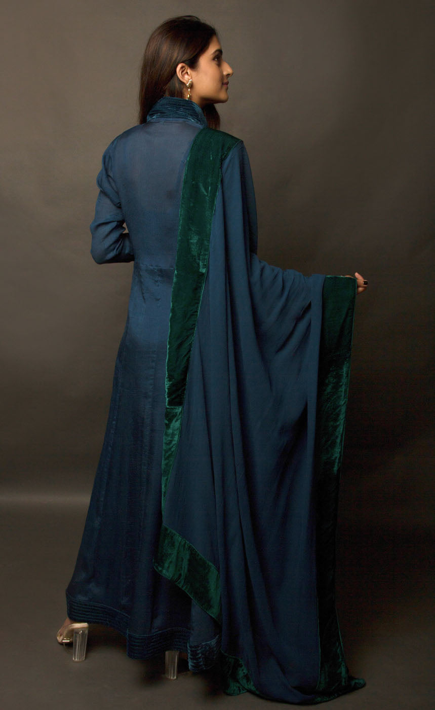 This is a beautiful plush velvet peacock blue-green long dress. It is a silk chiffon panelled dress with wrinkled sleeves, having a standing mandarin collar neckline and buttoned silk velvet placket. It is further lined with a taffeta slip having a cushioned yoke. It is accompanied by a silk georgette shawl finished with contrasting soft moss and sapphire black silk velvet borders.