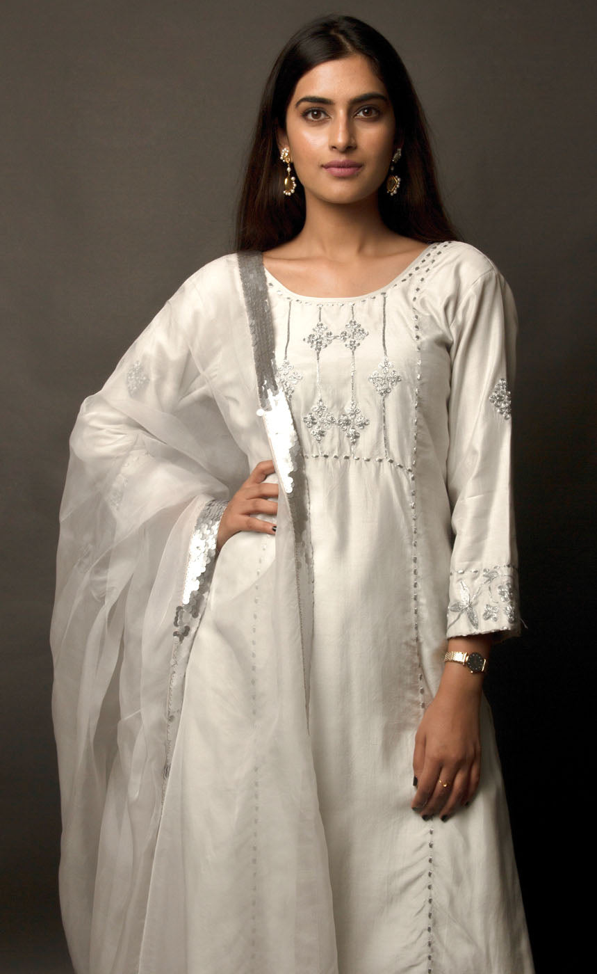 The muse is wearing a classic powder grey intricately embroidered kurta suit set with palazzos. The yoke panel, along with sleeve cuff and the palazzos bottom/cuff are delicately embroidered with silver-grey tilla. It is completed with a sheer organza dupatta carrying a matte grey hand-embellished sequin border.