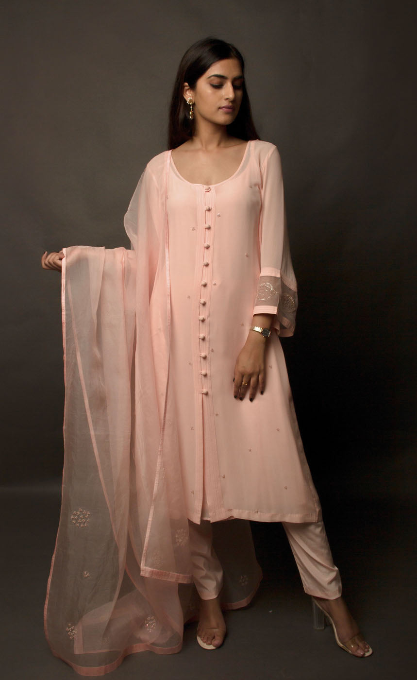 The muse is wearing a loop-buttoned suit set stitched in a lightweight georgette, minimally embellished with tonal glass beads in powder peach and translucent vibe.