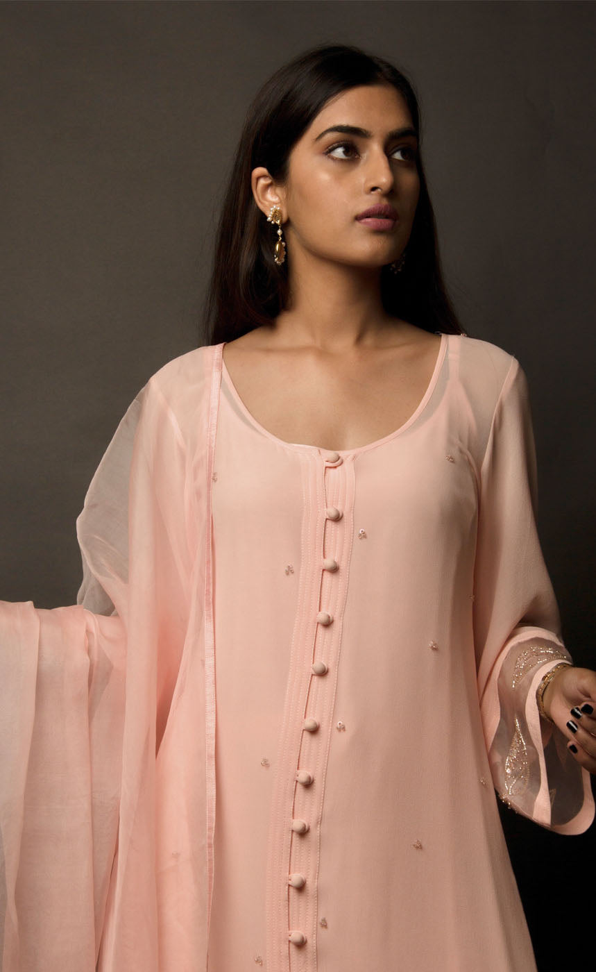 The muse is wearing a loop-buttoned suit set stitched in a lightweight georgette, minimally embellished with tonal glass beads in powder peach and translucent vibe.