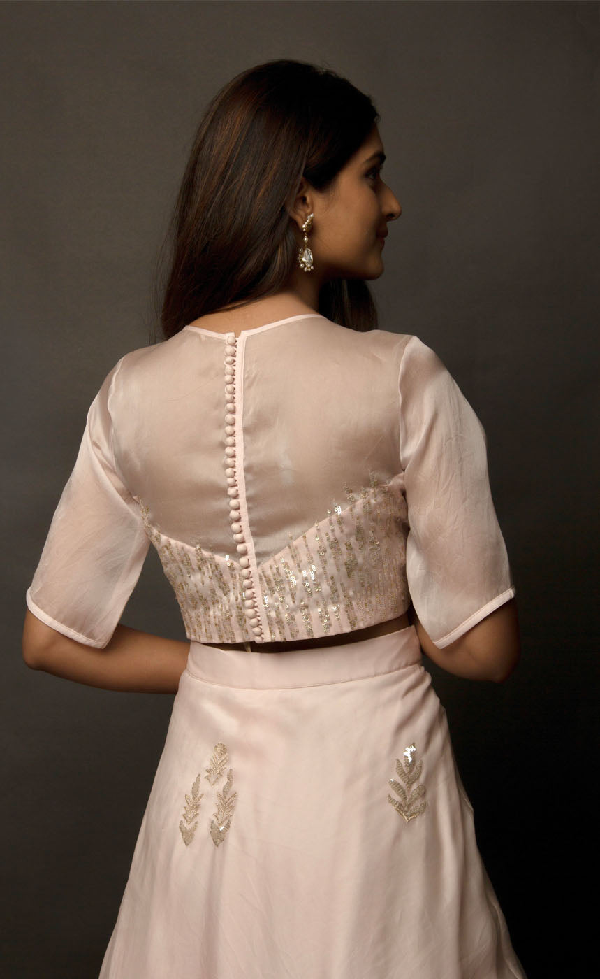 This dirty pale pink satin organza lehenga skirt is embroidered with zari and sequins motifs, the top is embellished with linear sequins and the coordinating silk organza dupatta is embroidered with sequin motifs finished with a raw silk border. 